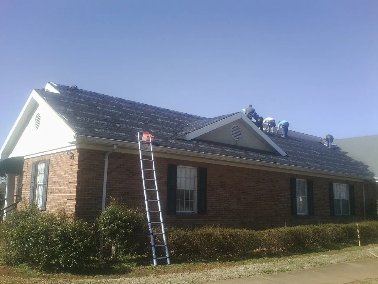 Crew tearing shingles off a brick ranch roof with a ladder set — Emergency Roof Repair work by our crew in San Leandro