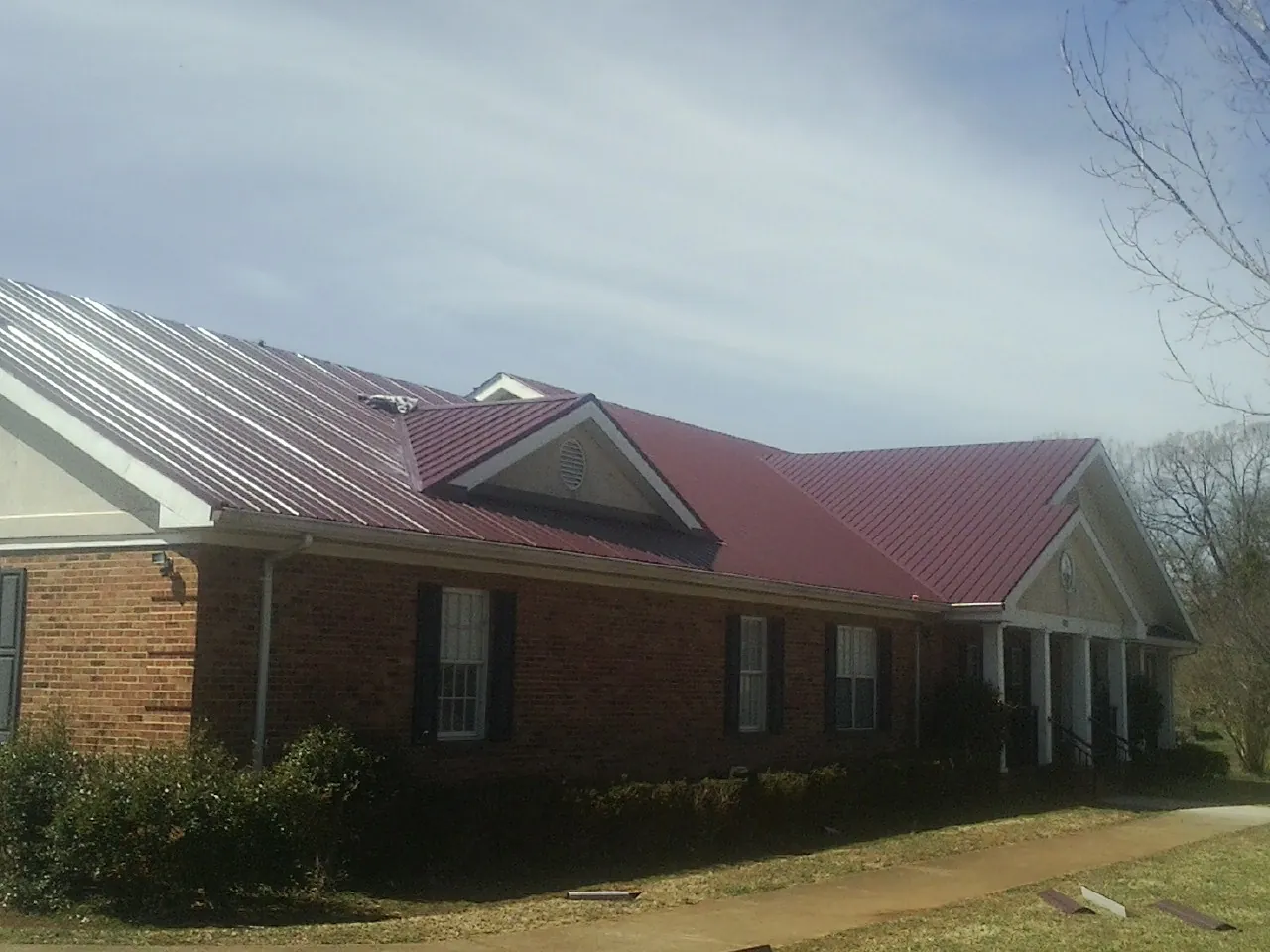 Red metal roof with gabled entries on a long brick building, from a Hail Damage Roof Repair job in San Leandro
