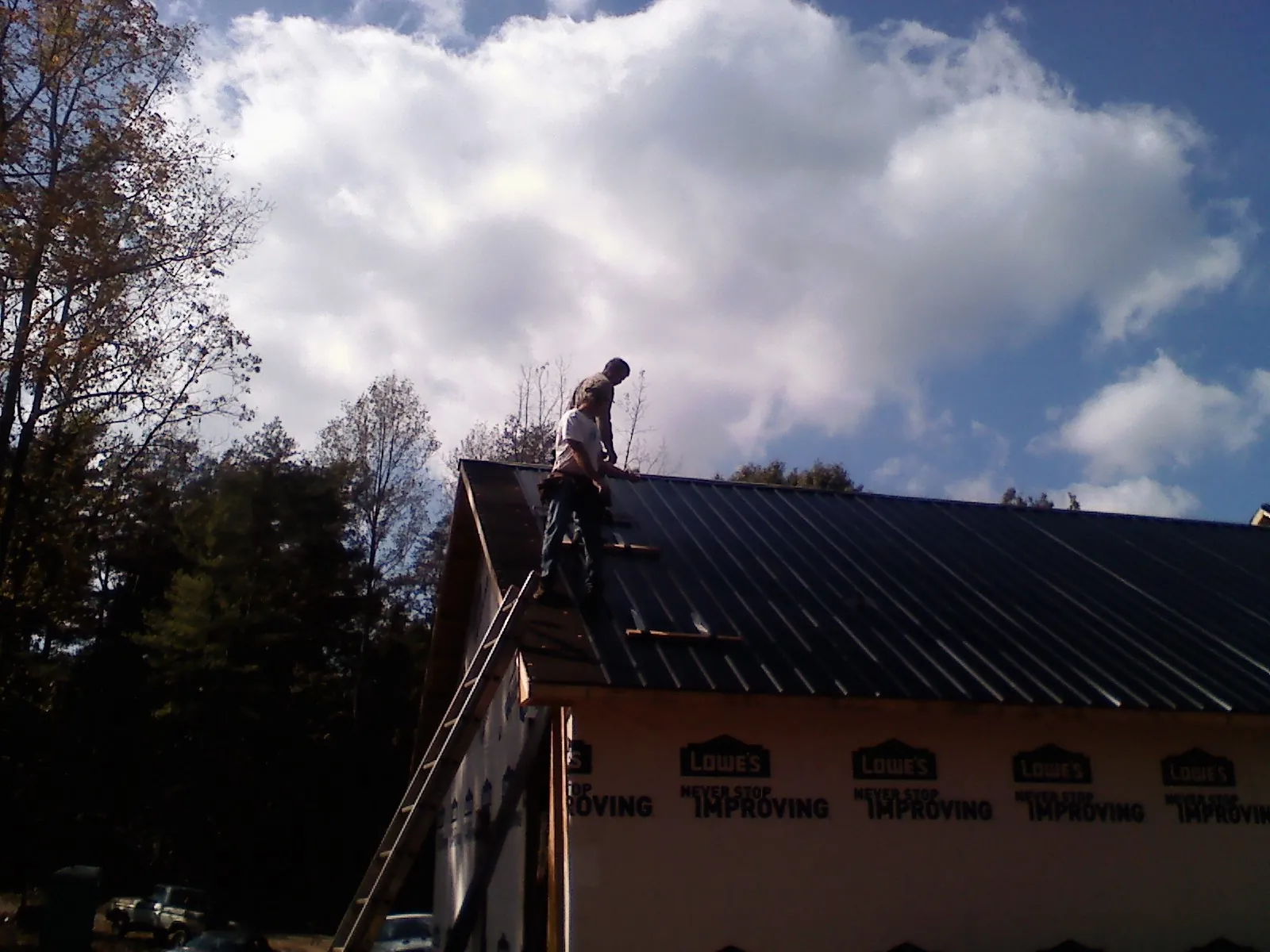 Roofer fastening dark metal panels high against a cloudy sky, from a Roof Inspection job in San Leandro